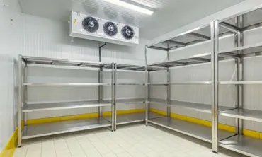 An empty white room contains metal shelving, tiled flooring, yellow base trim, and a wall-mounted unit with three fans.