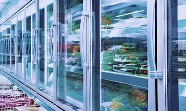A row of glass-door refrigerated display cases contains packaged food on shelves.