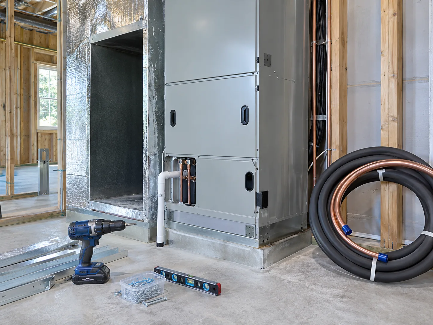 New air handler with ductwork, refrigerant lines, and installation tools.